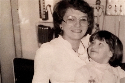 [ai] A black and white photo of a woman and a young girl smiling. The woman, wearing glasses and a white blouse, holds the girl, who looks up at her with a joyful expression.